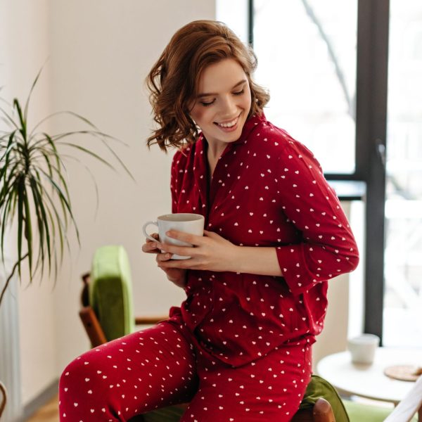 happy caucasian woman in pajama enjoying morning. indoor shot of winsome curly girl with cup of coffee